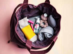 Open Pilates bag in mauve filled with neutral essentials — rolled towel, grip socks, facial spray, lip balm, and silk scrunchies — quiet luxury flat lay of Pilates bag essentials.