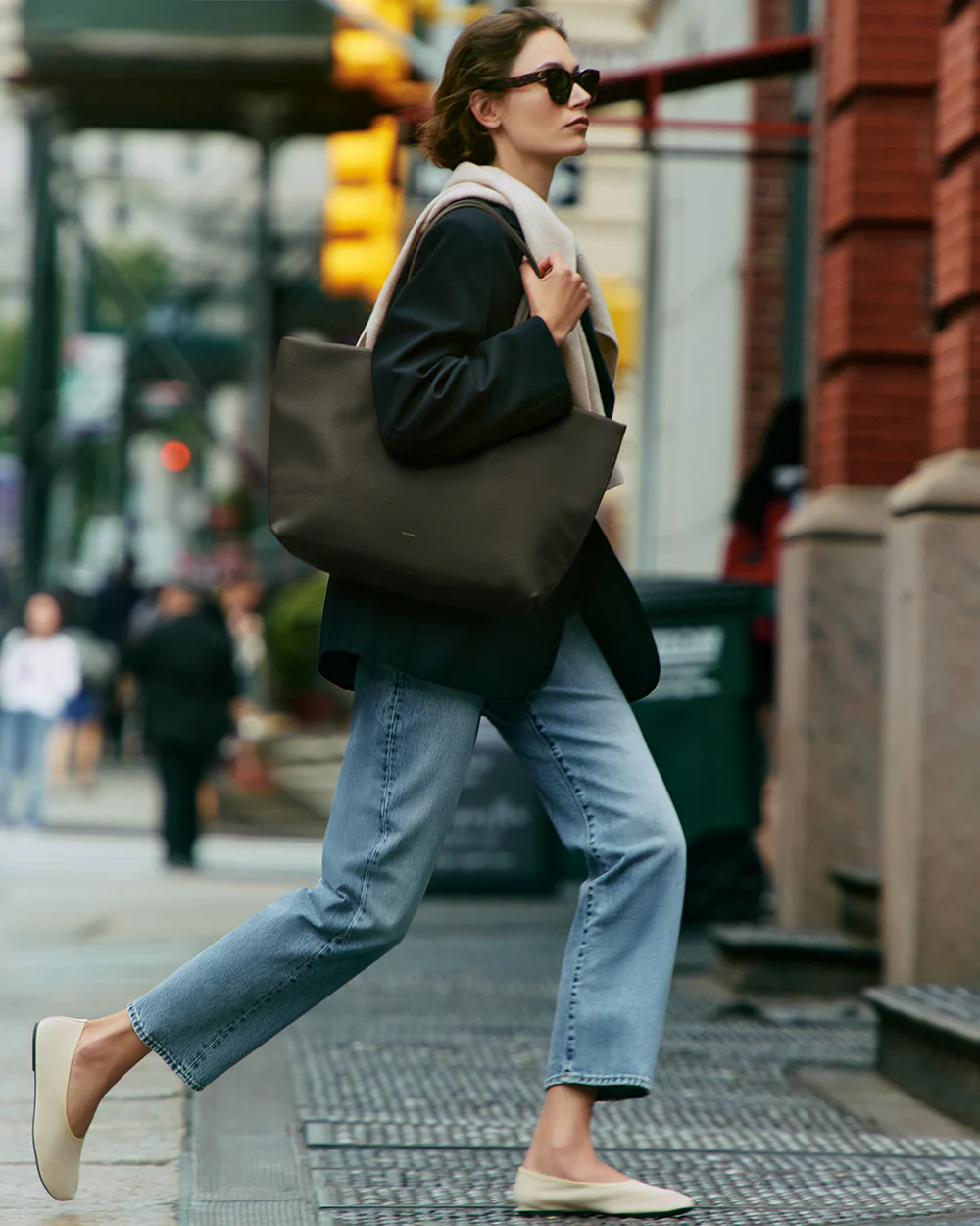 Woman wearing a neutral, elevated outfit with a black blazer, light wash jeans, cream flats, and a structured tote, demonstrating a cohesive color palette and polished everyday style.