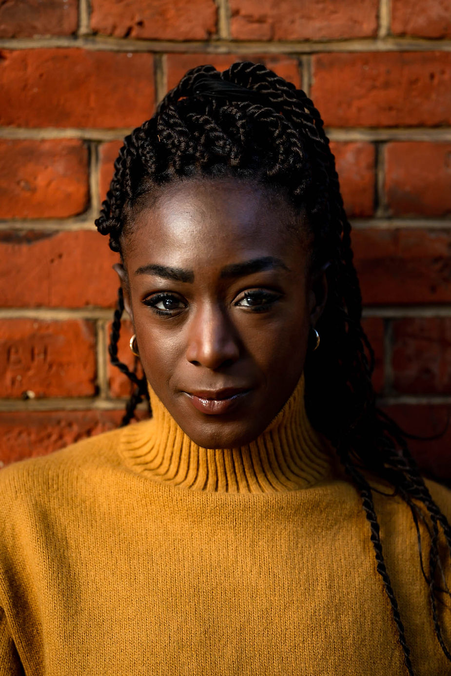A woman in a mustard jumper against a red brick backdrop