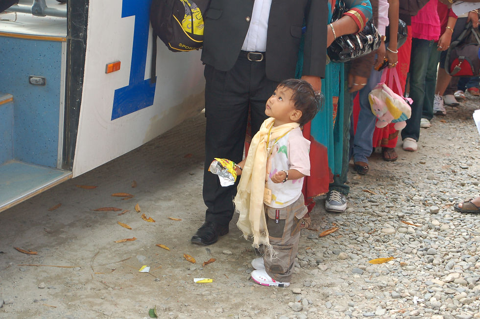 A small boy about to board an IOM bus. Behind him is a line of people. 
