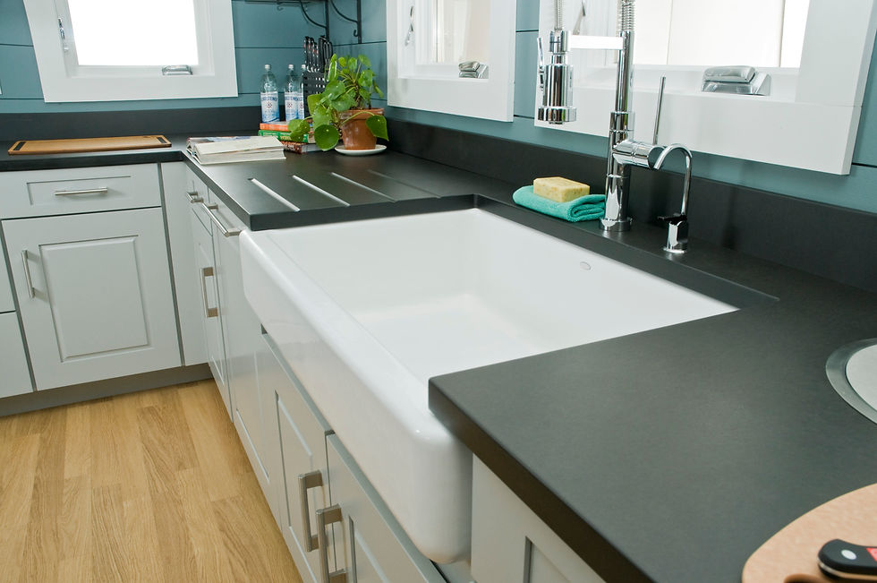 Modern kitchen with a large white farmhouse sink, Grays Harbor countertops, stainless steel faucet, potted plant, and wooden floor.