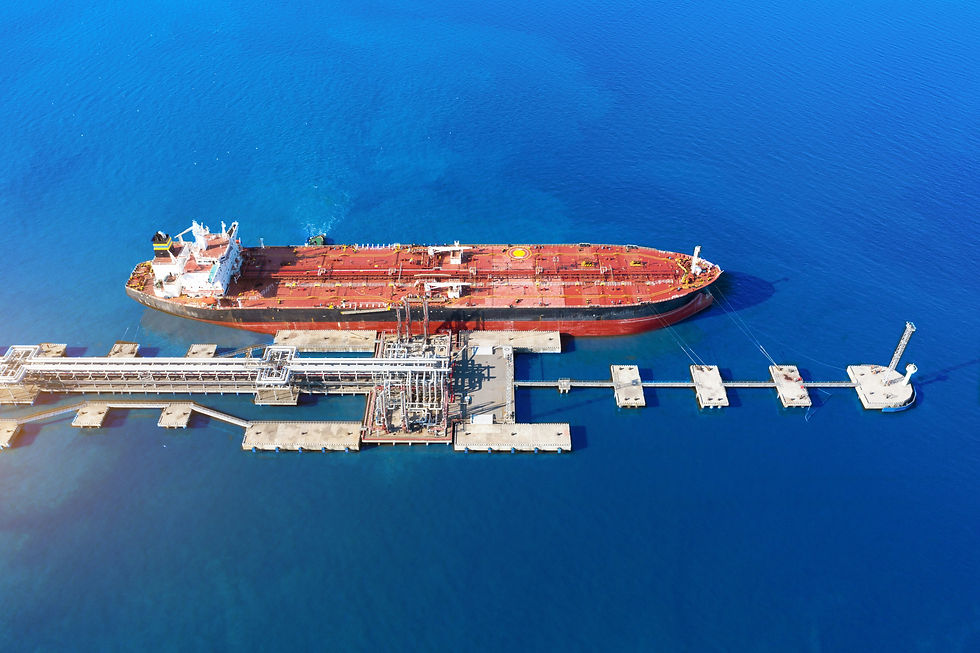 Aerial view of a large red and white oil tanker docked at an industrial marine terminal. The tanker is connected to the dock by multiple hoses, positioned against the vivid blue waters of the ocean, highlighting the scale and operation of maritime logistics.