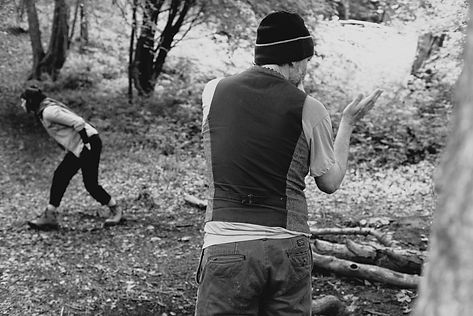 Man gestures in woods, woman walks away, black and white photo.