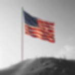 a realistic and simple image of an American flag posted on a dirt hill, with a clear sky i