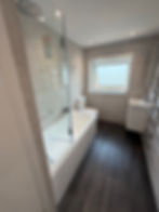 Modern bathroom with white tub, glass screen and dark floor