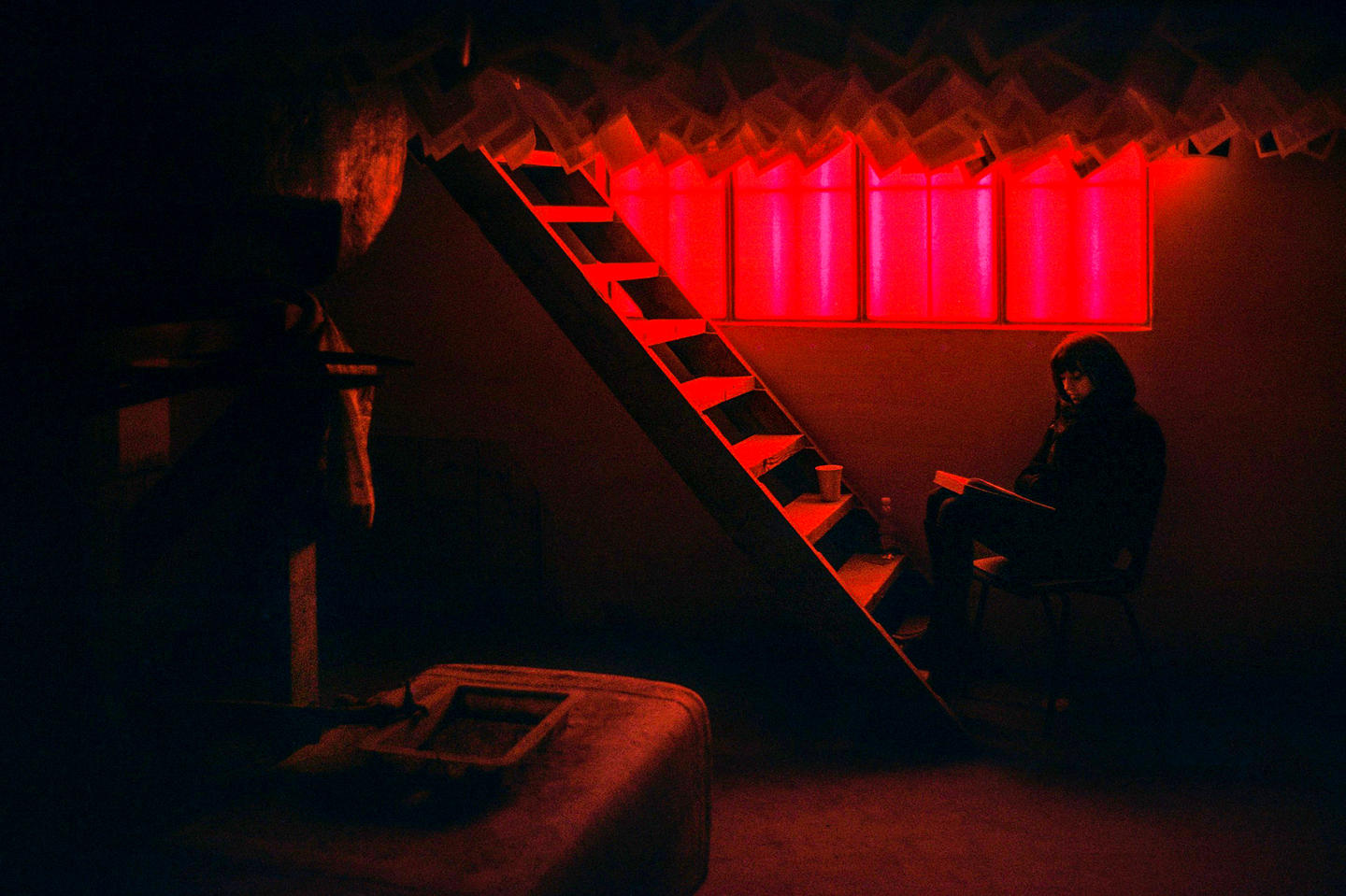 Captured from a scanned photographic negative, this image encapsulates a woman lost in time, she embodies the quiet essence of the moment, illuminated by filtered red light.