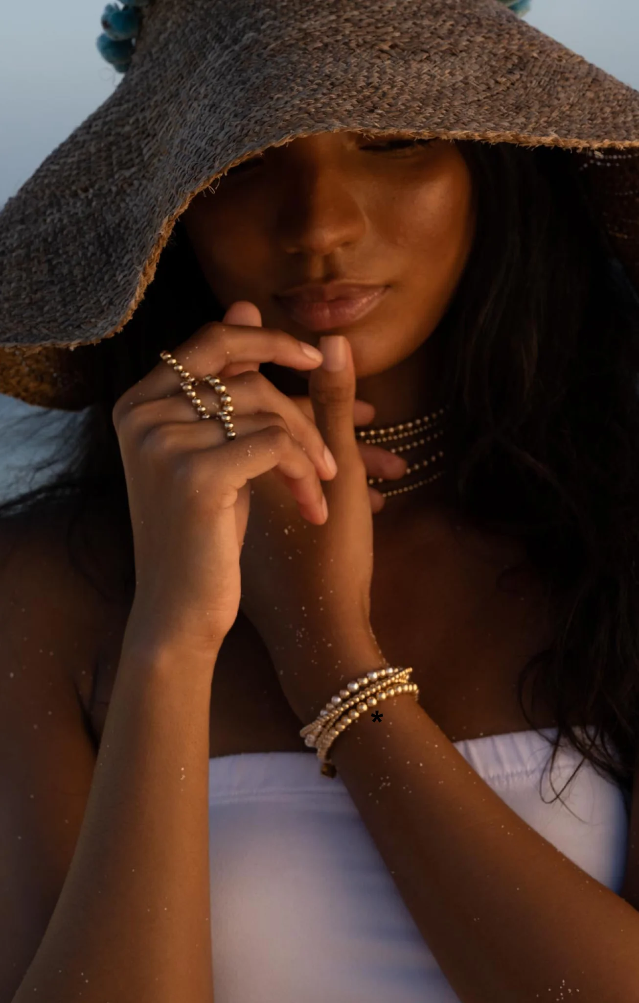 Moddel in beach hat wearing gold rings on finger and a gold bracelets on her wrist