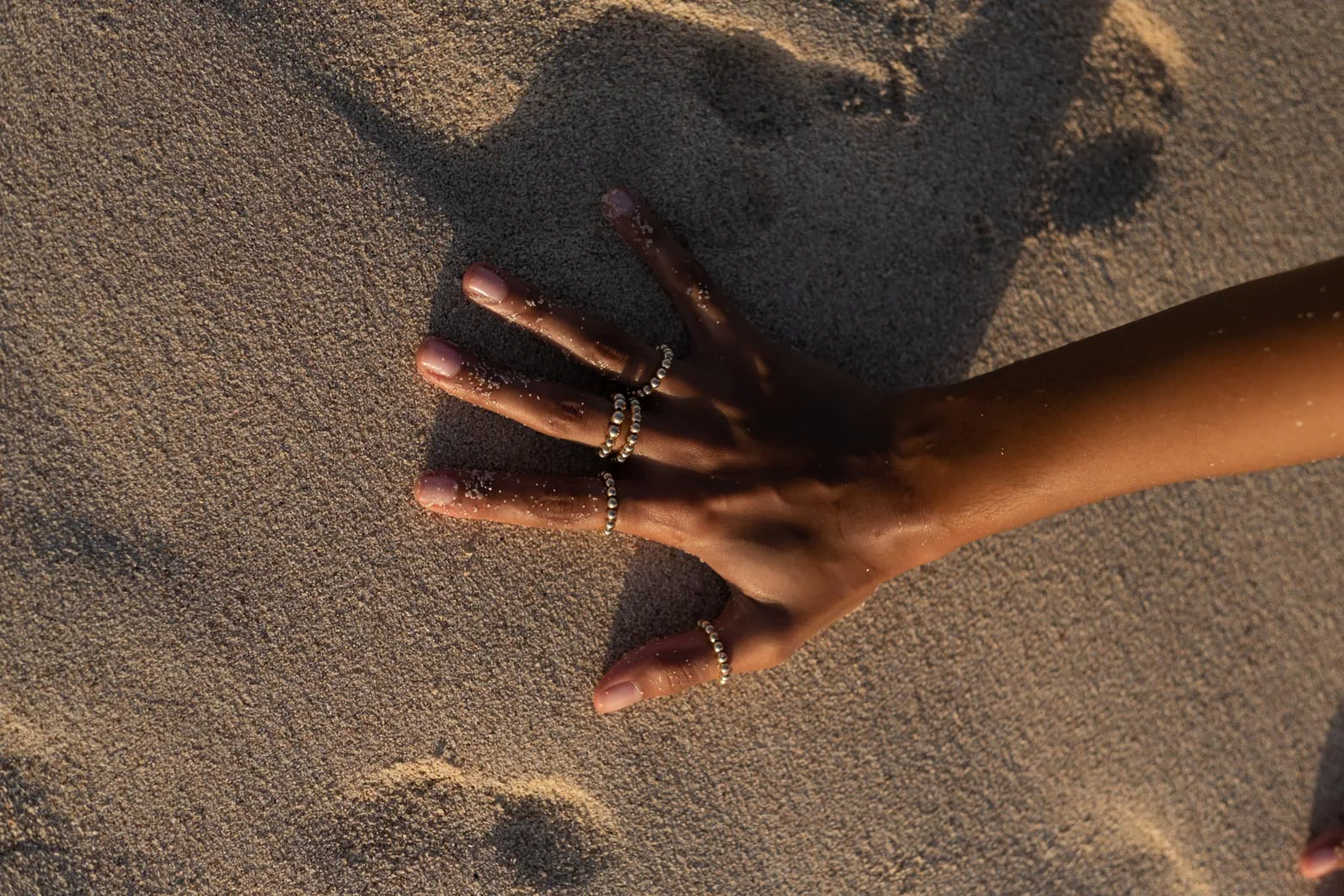 Hand spread on sand with gold rings on each finger