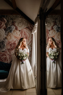A bride ready for a wedding at Kingscote Barn holding a bouquet of white wedding flowers, a moment of reflection looking out of the window before walking down the aisle