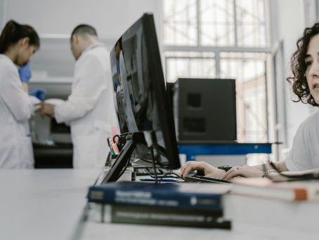 Focused woman working on a computer in a busy laboratory setting, showcasing teamwork and scientific research.