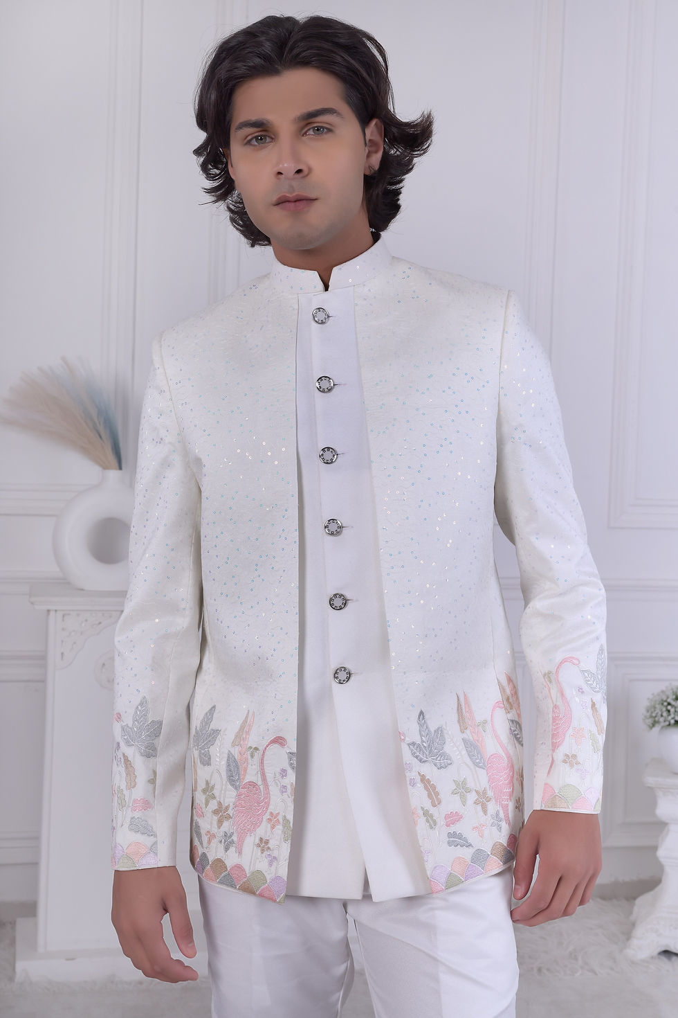 a man's designer white sherwani, showing the jacket's scattered shimmering sequins and the artistic pastel embroidery