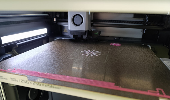 Imprimante 3D Bambulab en train d’imprimer les premières couches d’une toupie souffle avec du filament rose.