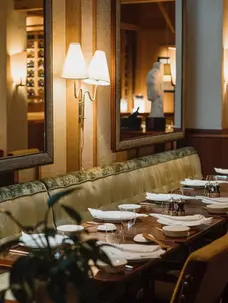 Restaurant tables laid with plates and cuttlery with green sofa and mirrors behind