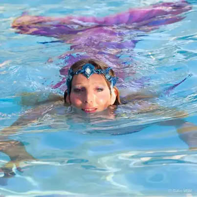 une femme sirène à la nageoire rose nage dans une piscine avec une couronne bleu 