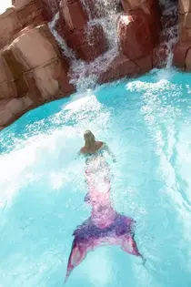Freya avec une queue de sirène violette et rose nageant vers une cascade