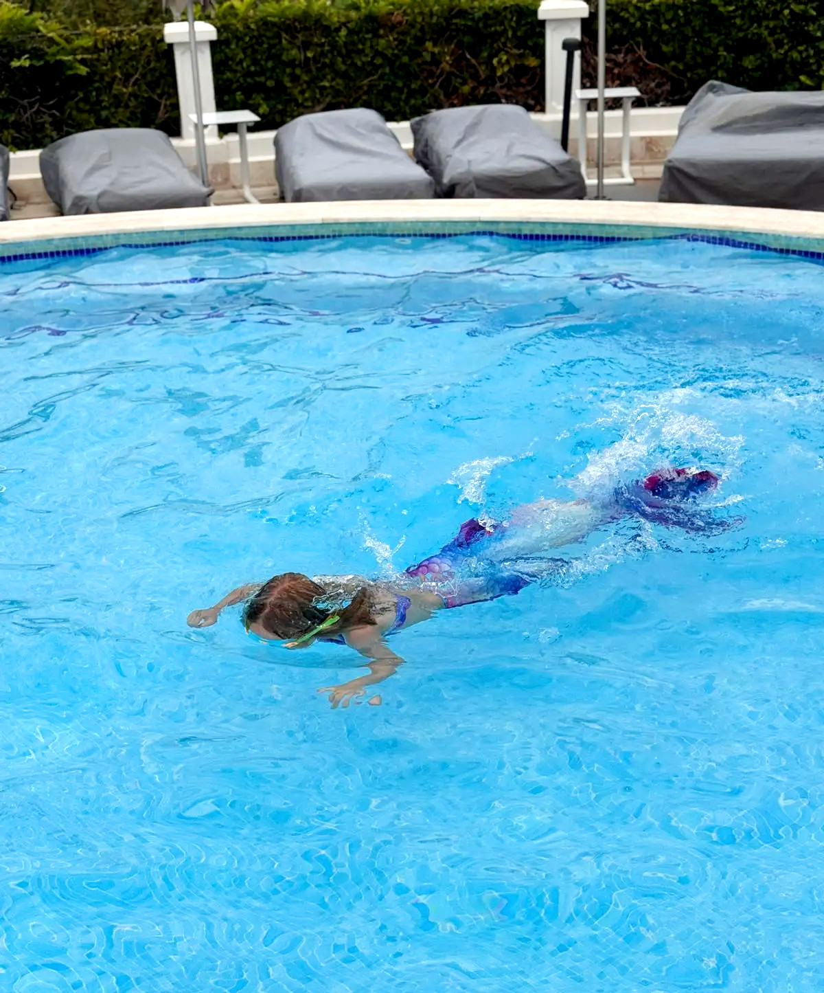 A child swimming in a pool with a mermaid tail