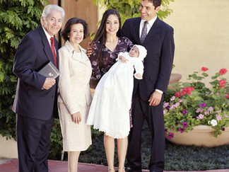 Two parents hold their baby in a baptism gown next to two older relatives.