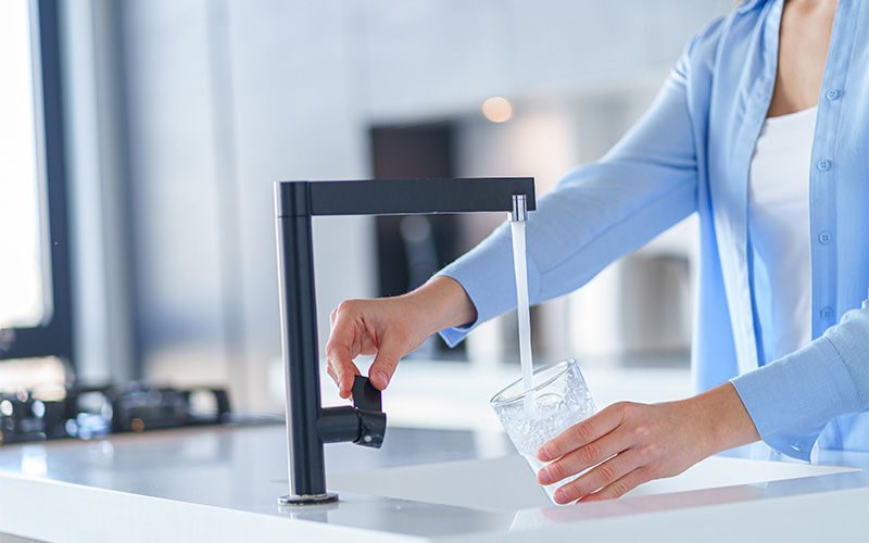 Person filling a glass with water from a kitchen faucet.