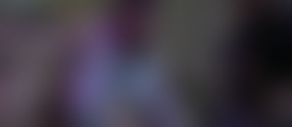 Man in white gi grappling on the ground, intense focus. Another pair sparring in the blurred background. Dim lighting, purple hue.