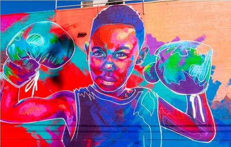 Vibrant mural of a young Black boy wearing boxing gloves, symbolizing strength, courage, and resilience in the fight for equity and community empowerment.