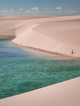 Em meio a dunas de areia, um lago de água azul esverdeado.
