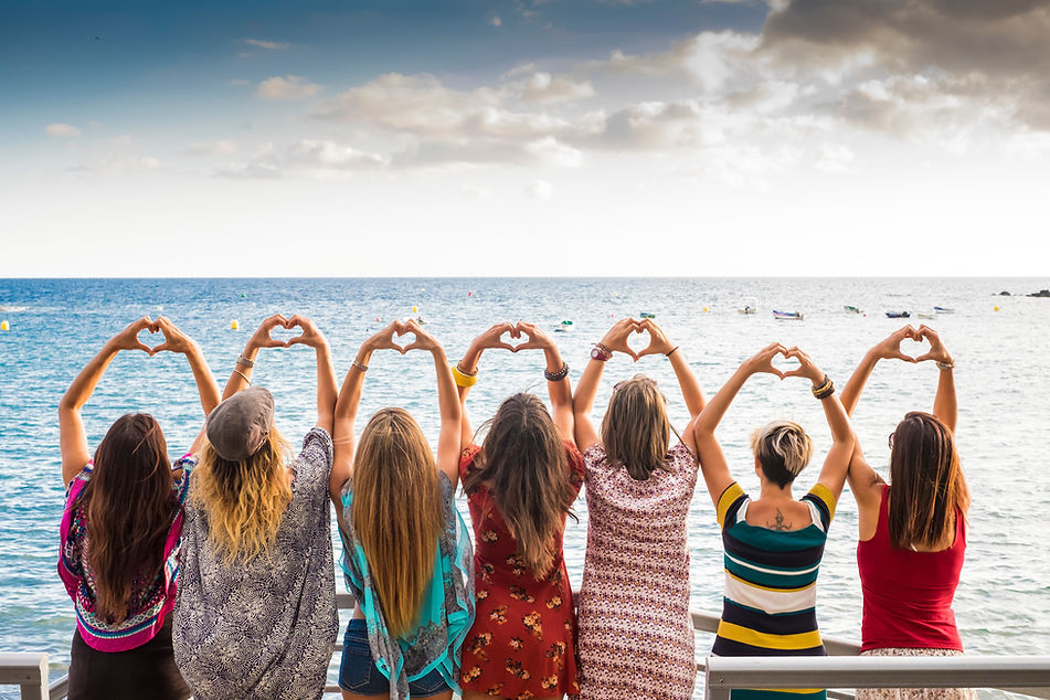 beautiful seven girls from the backside doing a heart with the hands looking at the ocean