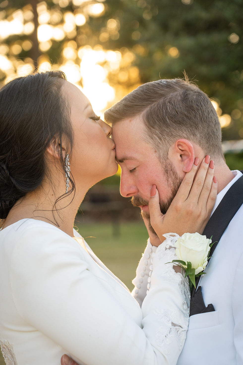 Bride kisses groom's forehead with sunset behind them