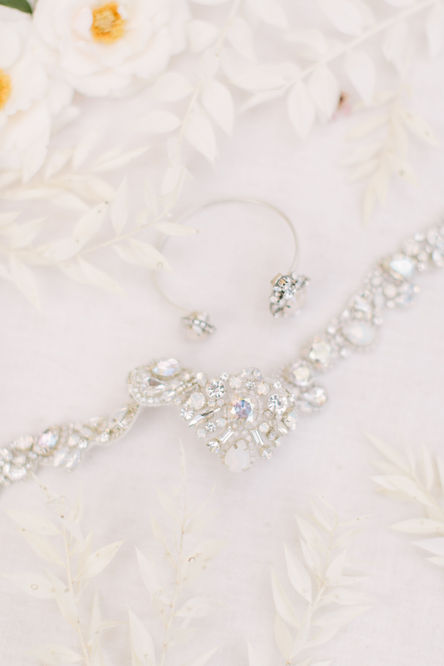 Add a short description of an image of a Wedding planned by A Stephens Soirée to improve your site’s SEO and accessibility. The image contains a detailed shot of the jewery the bride wore during the wedding. There are small white flowers with touches of yellow present in the photo.