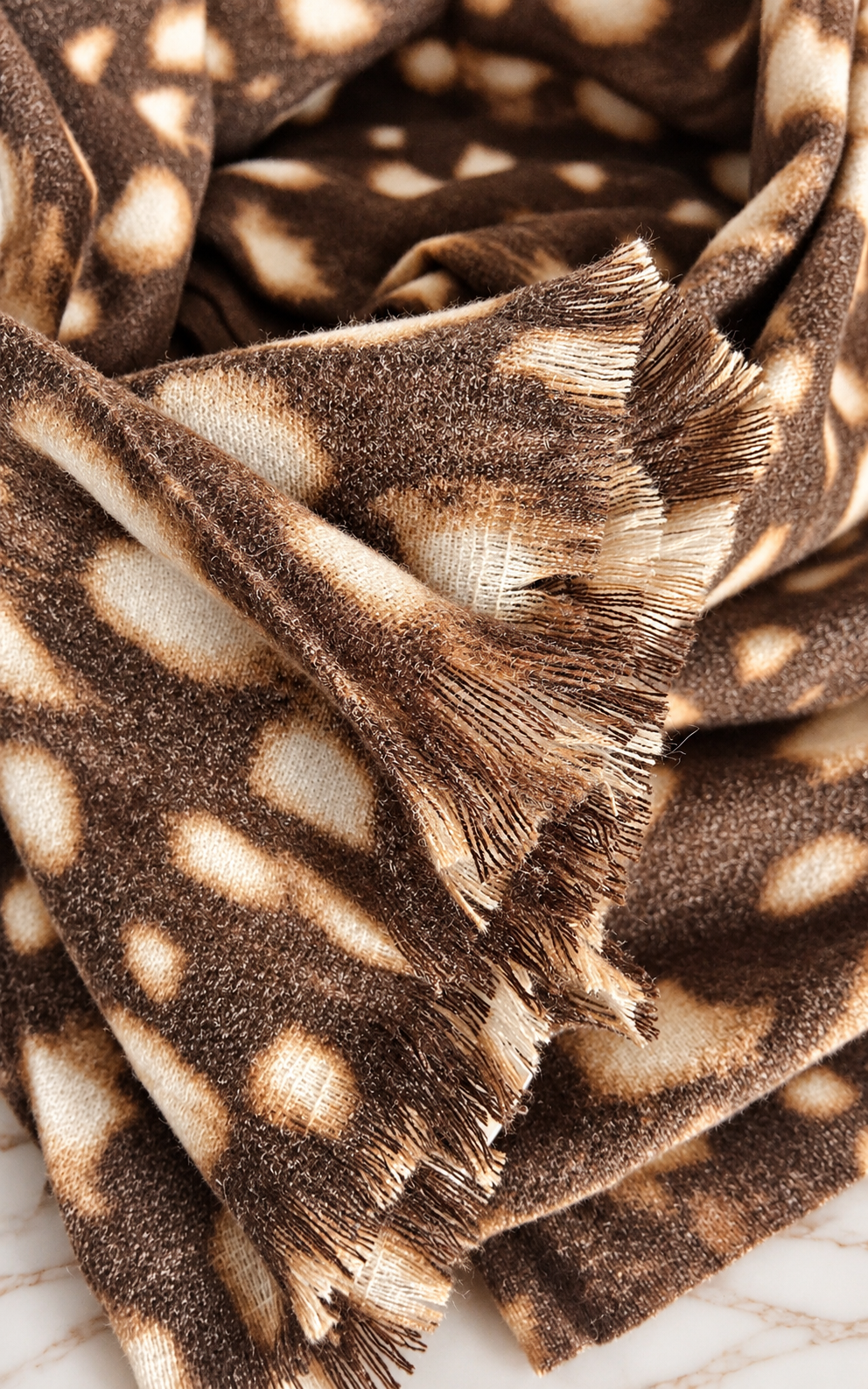 Close-up of chocolate brown deer print cashmere blend scarf showing soft fabric texture and delicate fringed edges.