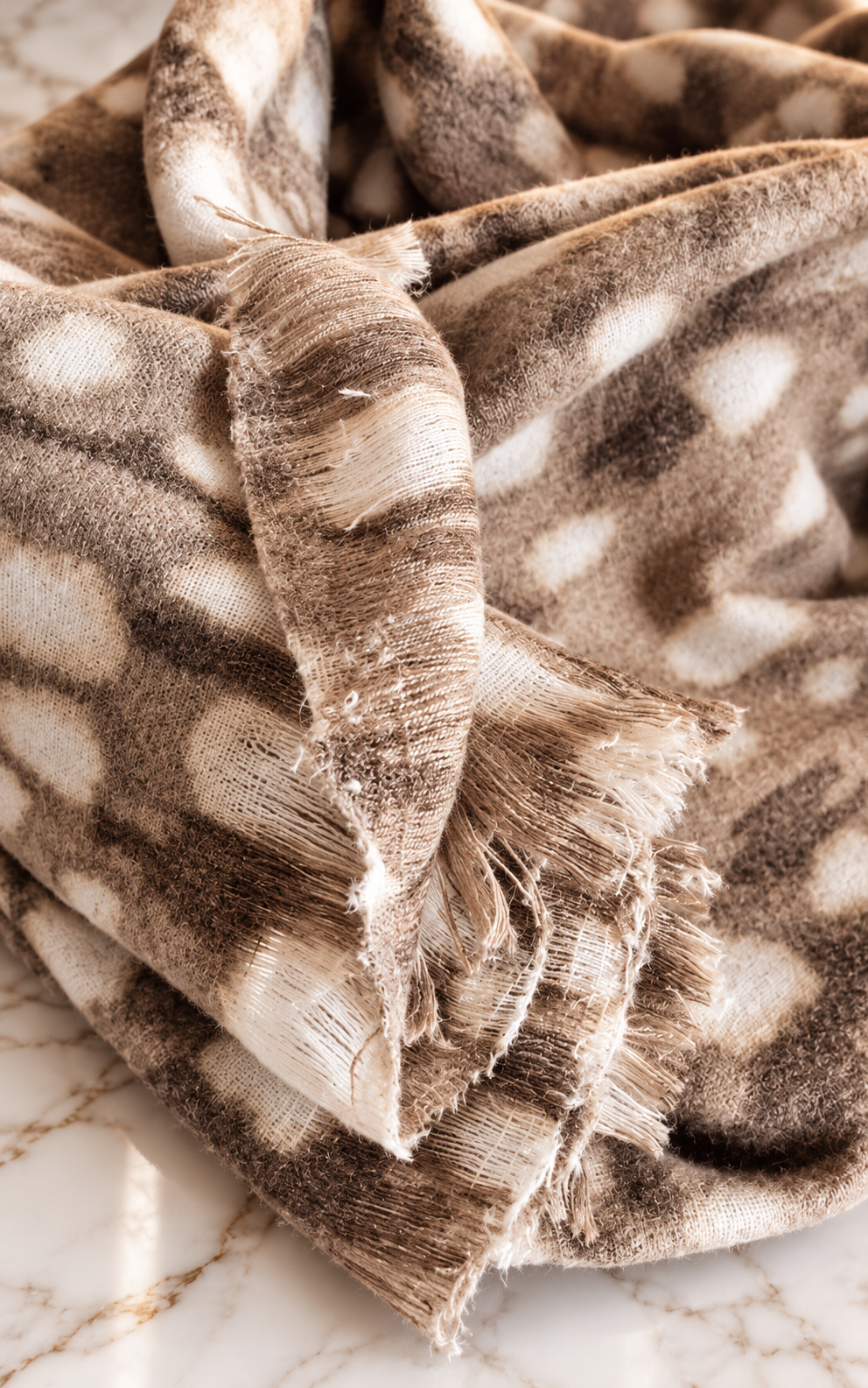 Close-up of taupe deer print cashmere blend scarf highlighting its soft woven texture, fawn pattern and frayed edges.