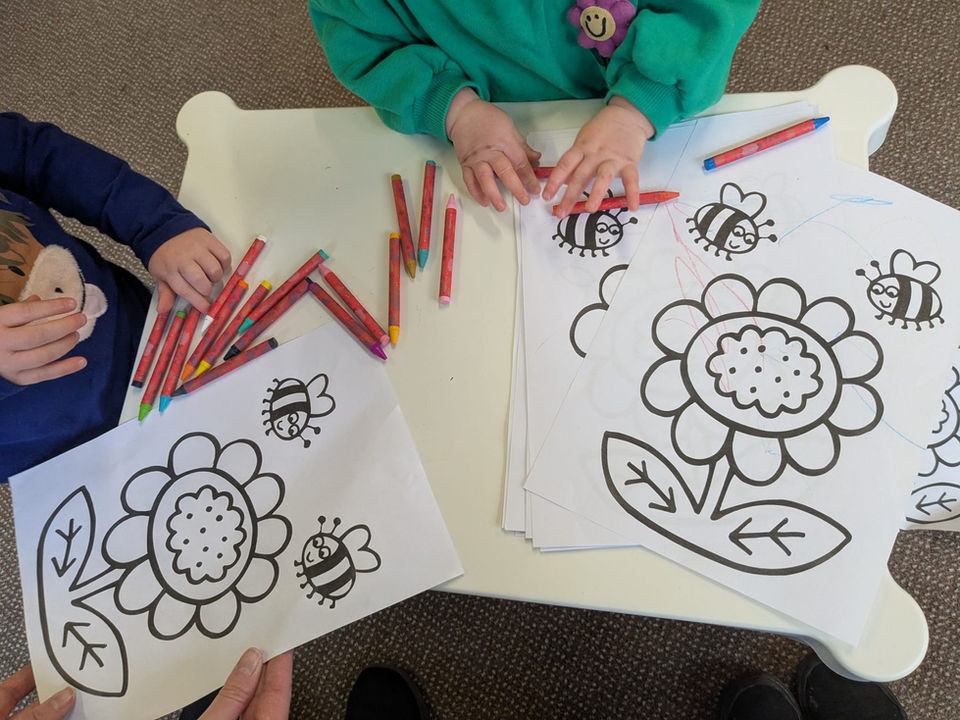 A colouring in table with outline pictures of flowers, crayons and some childrens hands