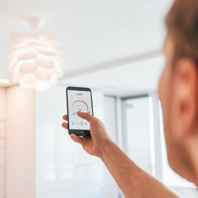 Person using a smartphone app to control a white ceiling light in a modern, bright room. The phone screen shows light settings.