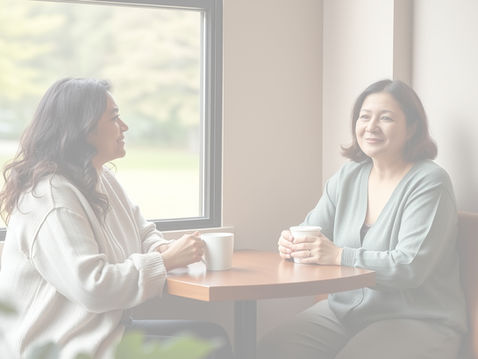 Two women sitting together over coffee in a calm café, sharing a quiet conversation that reflects support and a sense of not carrying everything alone