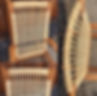 Olsen rocking chair with intricate woven rattan seat and backrest in a light tan hue. Set against a wooden fence and gravel ground.