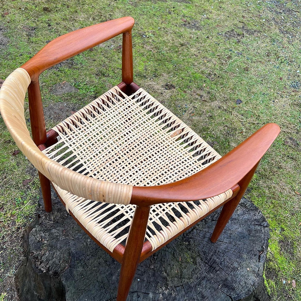 Wegner Round Chair with a binding cane woven seat on a tree stump. The chair has a natural finish, and the ground is covered in grass and moss.