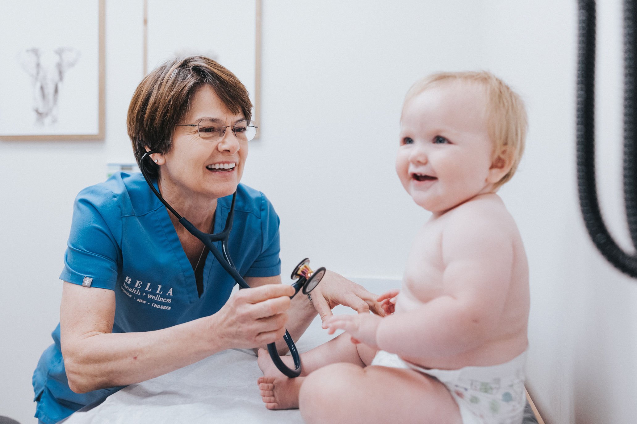A Bella Health + Wellness clinician using a stethoscope with a baby.