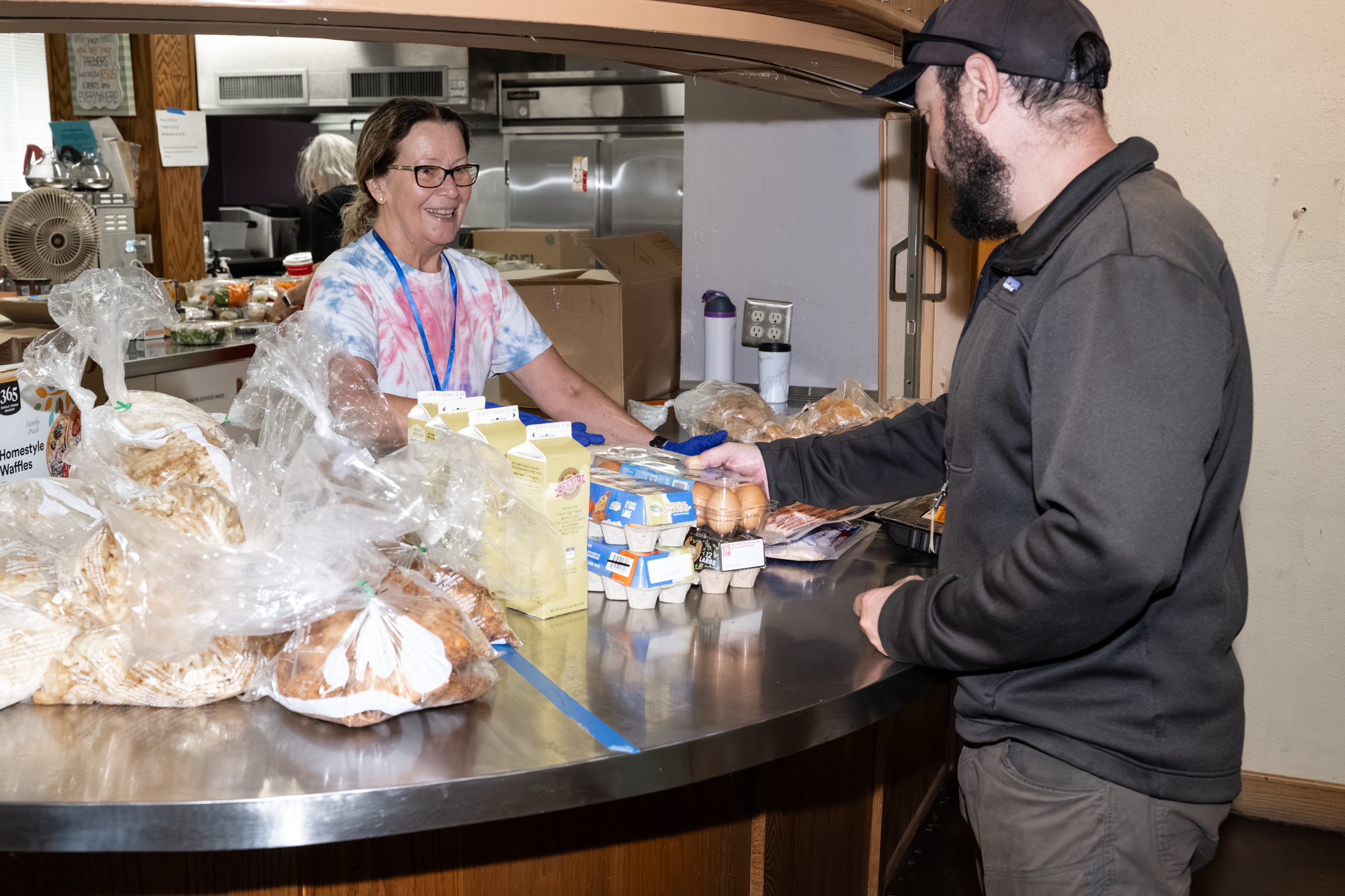Two people at a Covenant Cupboard food counter with bread, milk and eggs.