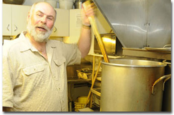 A man stirring a large cooking kettle in a kitchen.