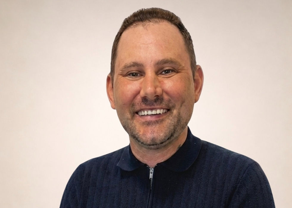 Smiling man wearing a dark blue zip-up shirt against a neutral background. Appears cheerful and friendly.