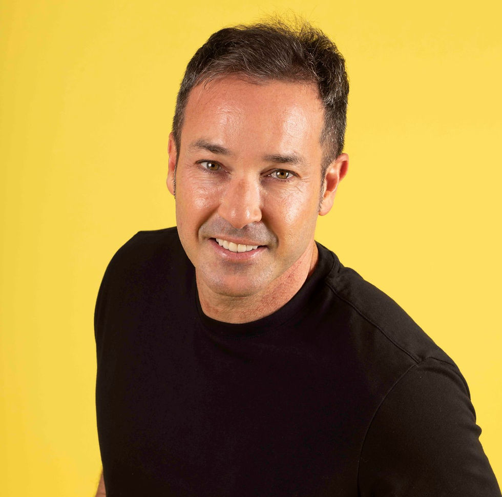 Smiling man in a black shirt against a bright yellow background, conveying a cheerful mood.