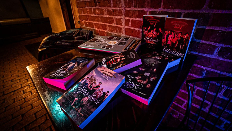 Books displayed on a wooden table against a brick wall, lit by dim, colorful lighting. A laptop and a backpack are nearby.