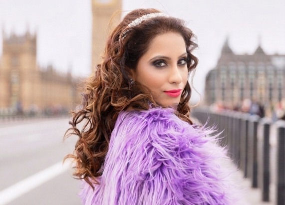 Woman in a purple fur jacket poses confidently on a bridge. Iconic buildings in the background. Overcast sky adds a dramatic mood.