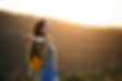 Woman with outstretched arms and yellow backpack basks in sunset on grassy hill. Serenity and freedom in nature are captured.