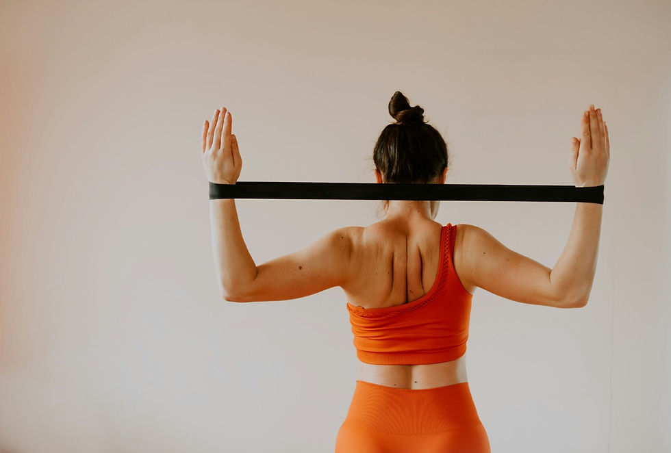 Woman in orange athletic wear exercises with a black resistance band, arms raised. Neutral background, focused and calm mood.