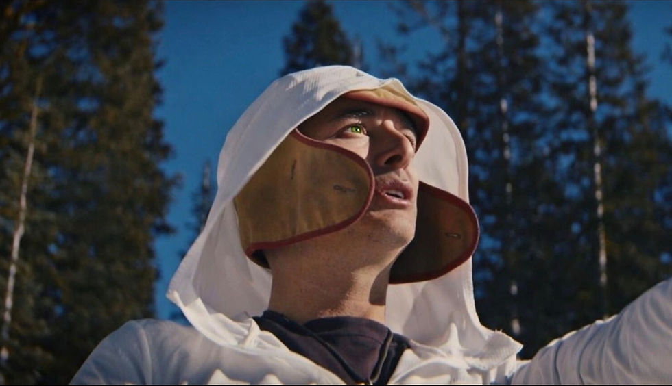 Person in a white hood looking up, with trees and blue sky in the background. A sense of focus and determination is evident.