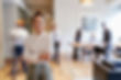 A confident woman stands smiling in the foreground of a modern, open-plan office while coworkers move and collaborate in the background.