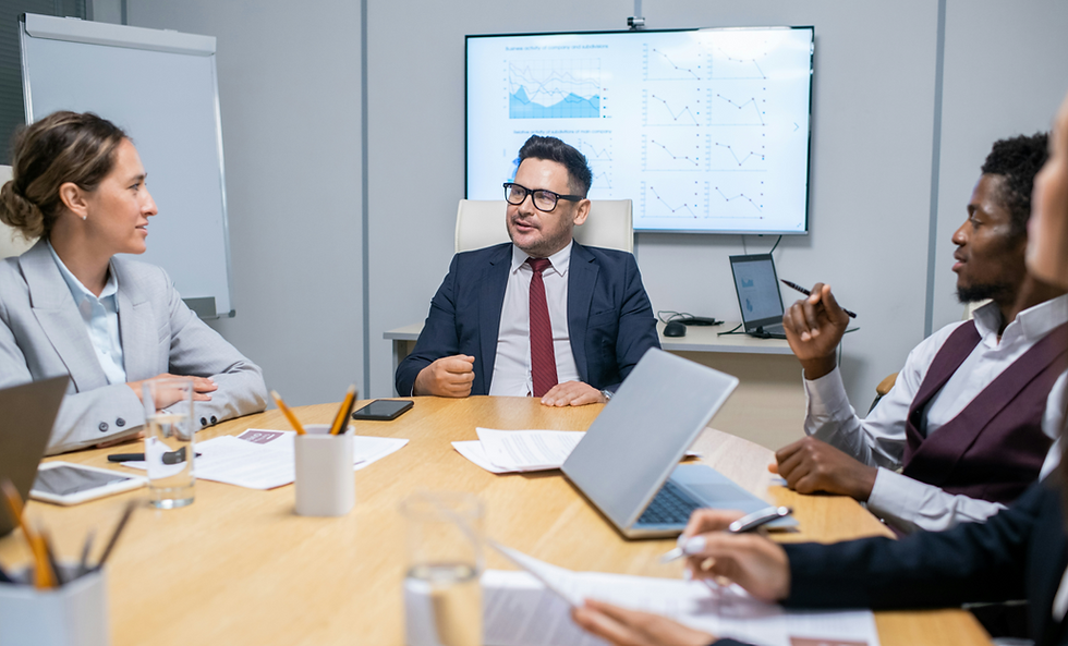 Business meeting with four professionals around a table, discussing charts on a wall screen in a modern conference room.