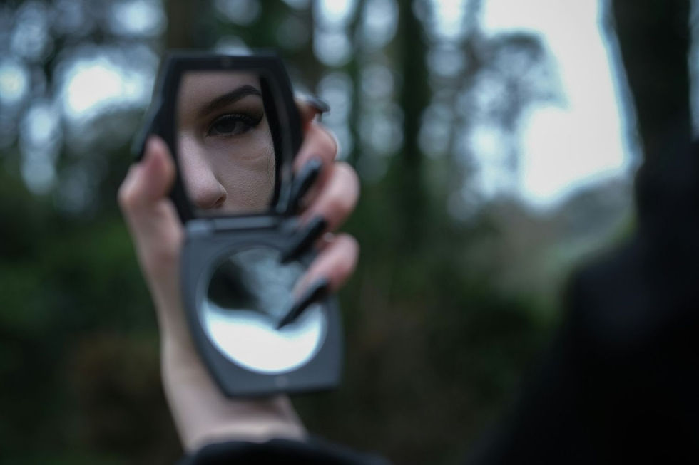 Hand holding a compact mirror reflecting an eye, set against a blurred, green forest background. Mysterious and moody atmosphere.