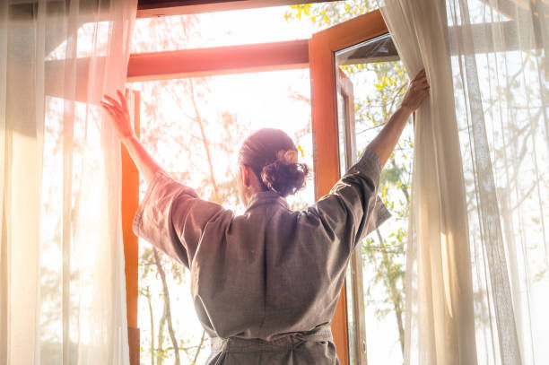 woman opening her bedroom curtains after waking up
