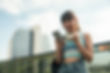 A young woman smiles excitedly while looking at her phone and holding headphones outdoors in the city.